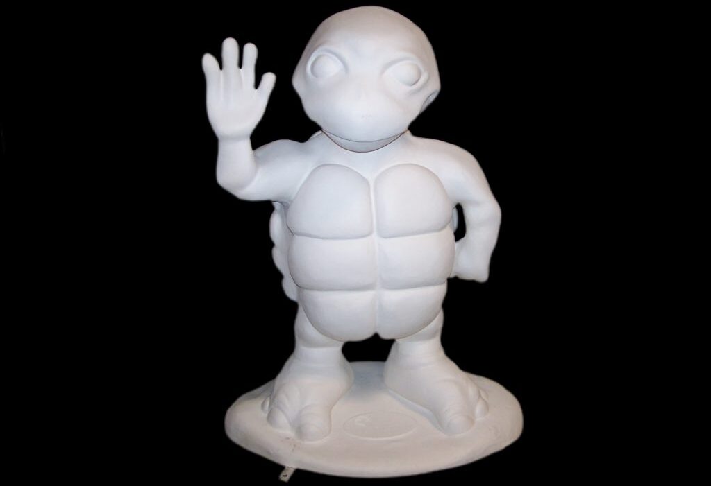 Front view of a waving cartoon turtle fiberglass sculpture on black background.