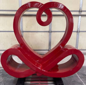Front view of a glossy red custom fabrication sculpture featuring a heart-shaped top and flowing base loops